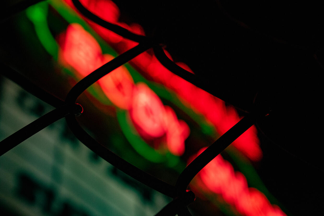 Perspective Shot Abstract blurry red neon sign with green accents behind a dark wire fence.