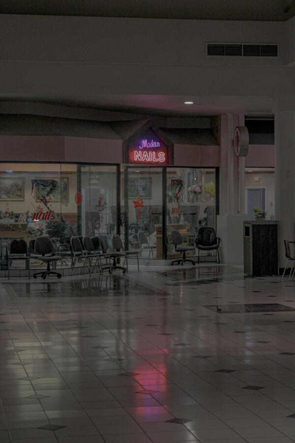Old Mall Shot Neon sign reading "Modern Nails" above the entrance to a nail salon inside a dimly lit shopping mall, with rows of empty chairs in the waiting area.