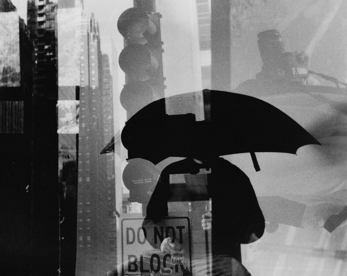 Dark Room Work Abstract double exposure of a person holding an umbrella on a city street with a traffic light and buildings.