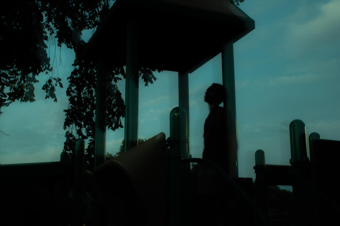 Night Shot Silhouette of a person leaning against a pillar on a playground structure against a cloudy sky.