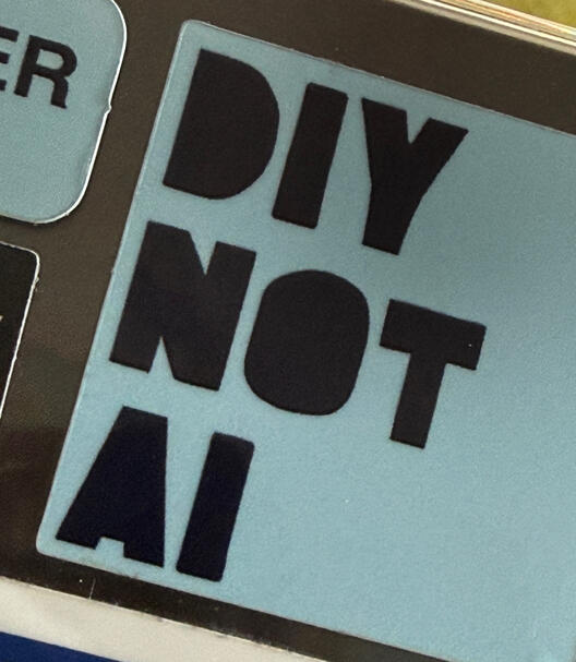 Sticker with text "DIY NOT AI" in black block letters on a light blue background.