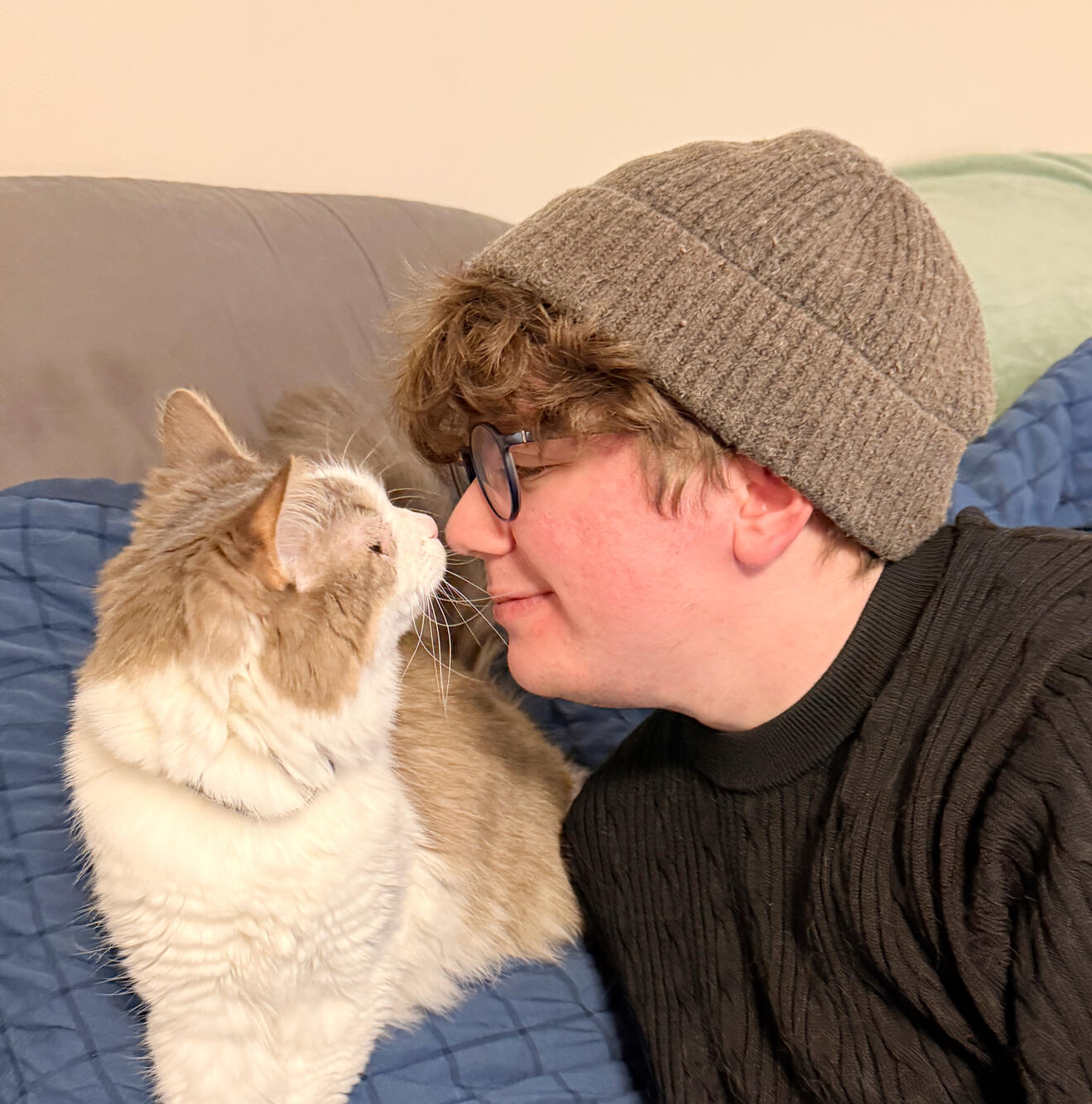 Liam with a gray beanie and glasses with a light and fluffy cat, the cat and him touching noses.